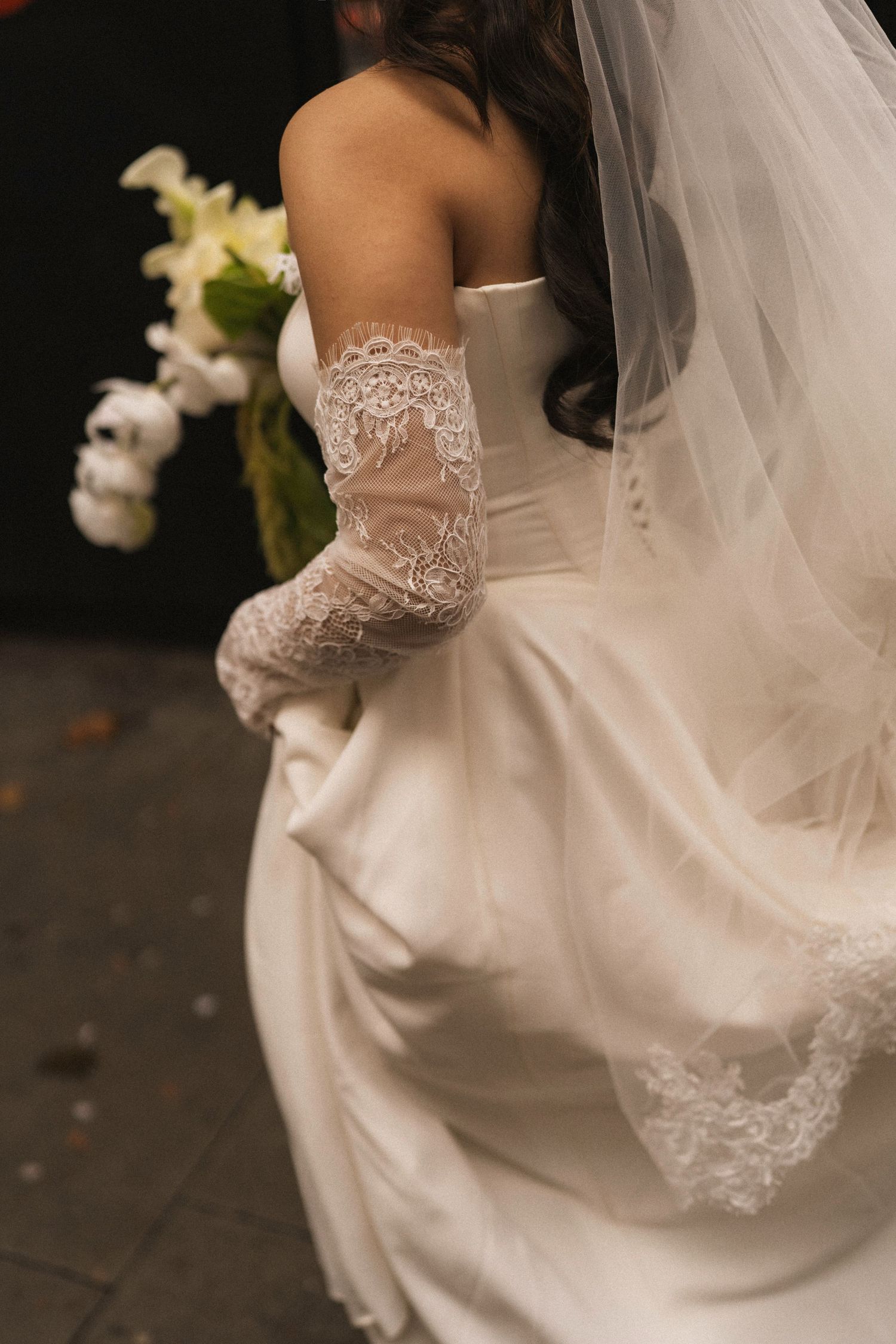 Close-up details of delicate lace trim and flowing fabric on a white wedding dress with sheer veil.