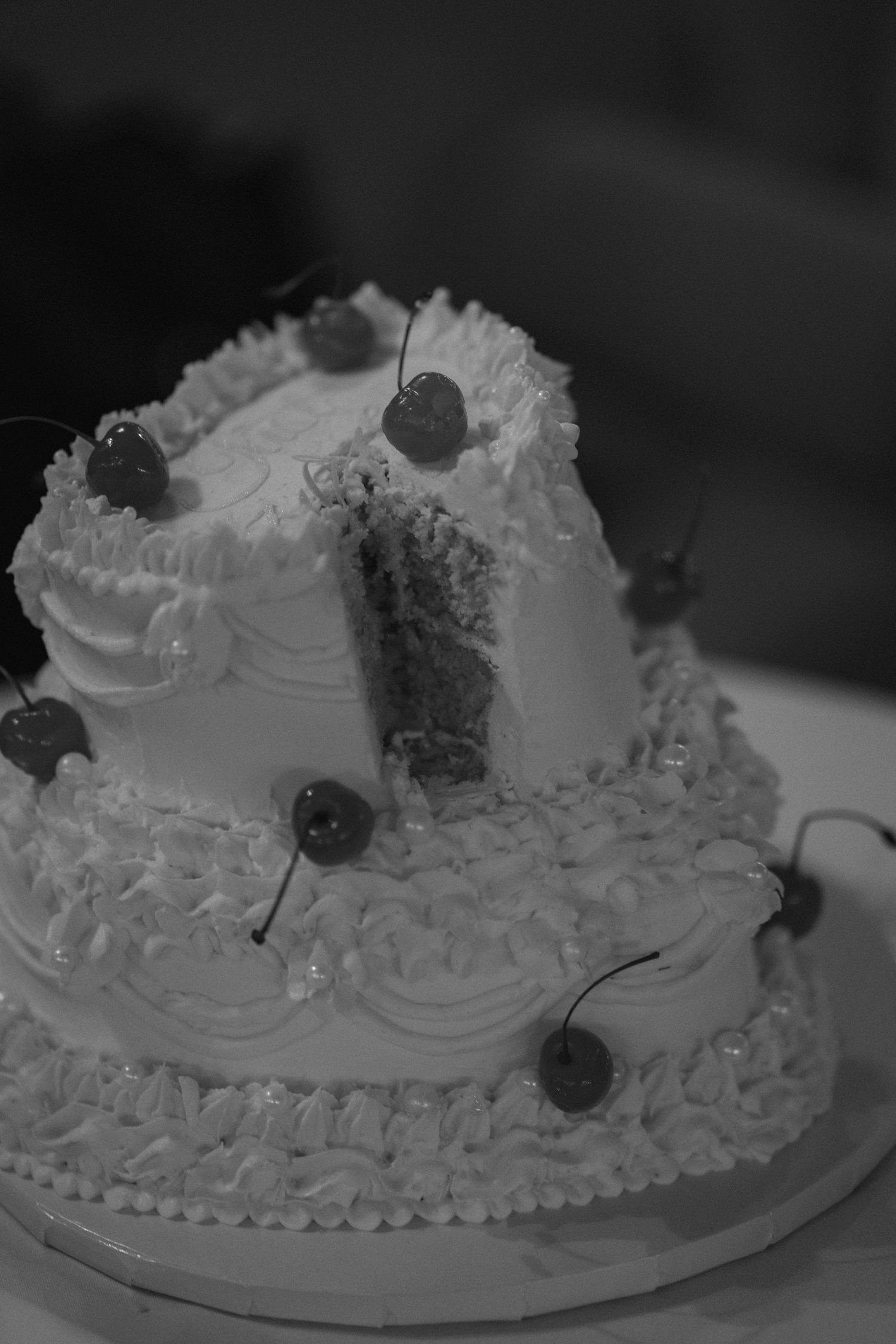 Black and white close-up shots of a decorated white frosted cake with dark berries arranged in sequence.