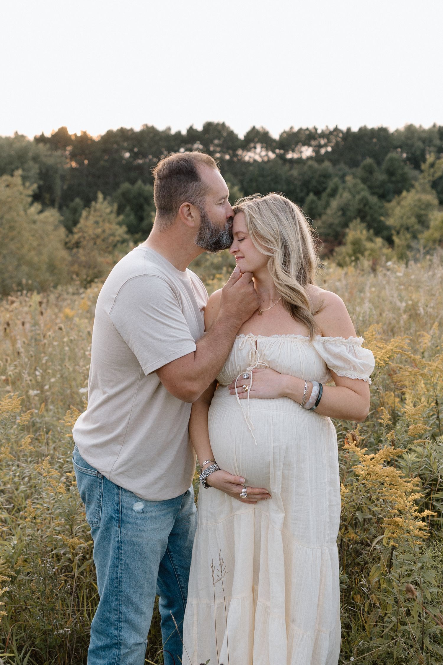 A couple shares an intimate moment in a wildflower field during a maternity photoshoot.