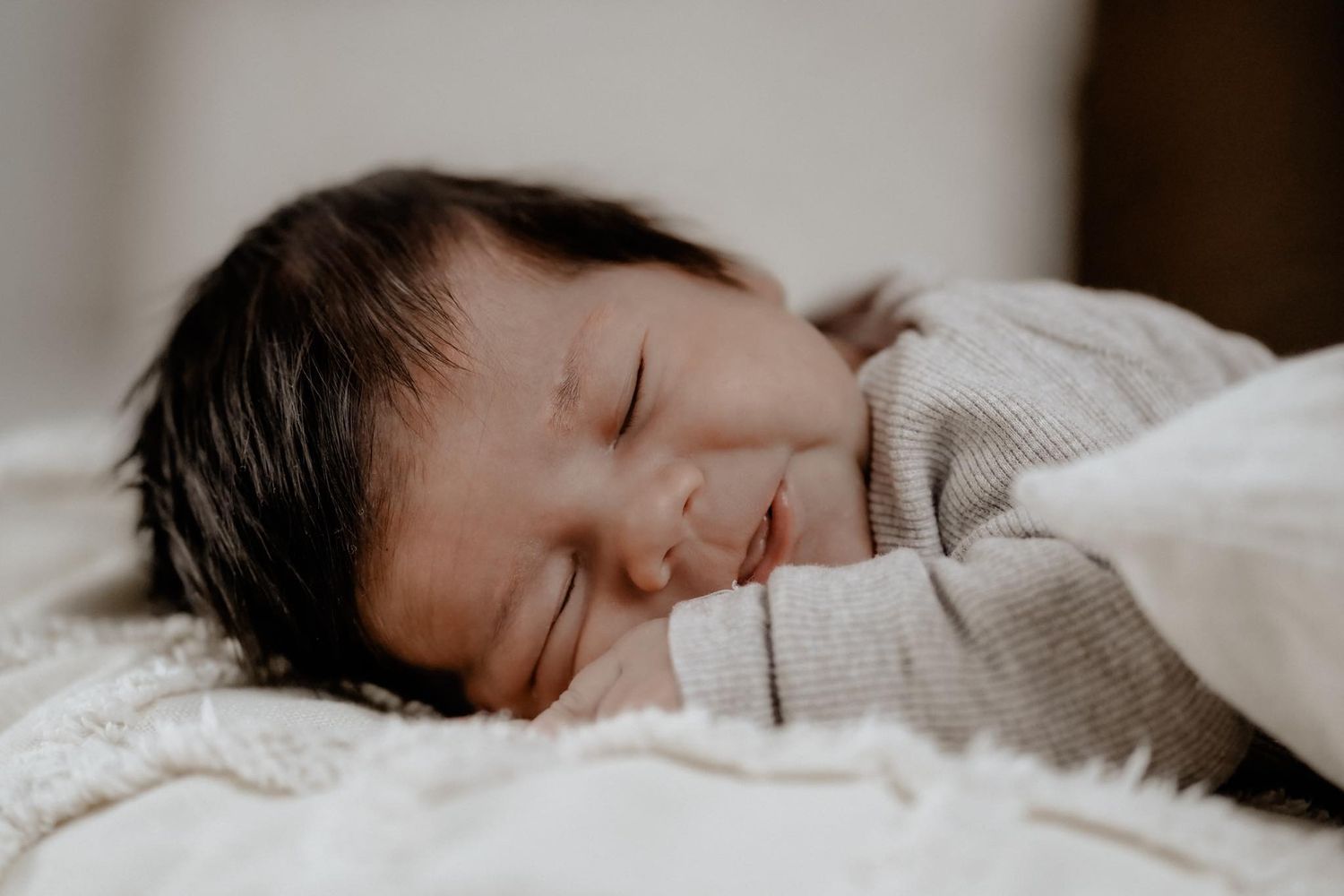 Baby sleeps peacefully on soft white bedding while sunlight gently filters through nearby window.