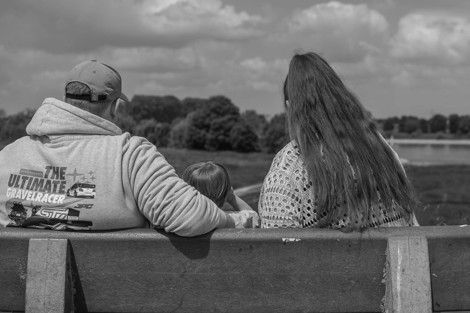 A series of black and white moments of people relaxing in park benches, taken from behind against a cloudy backdrop.