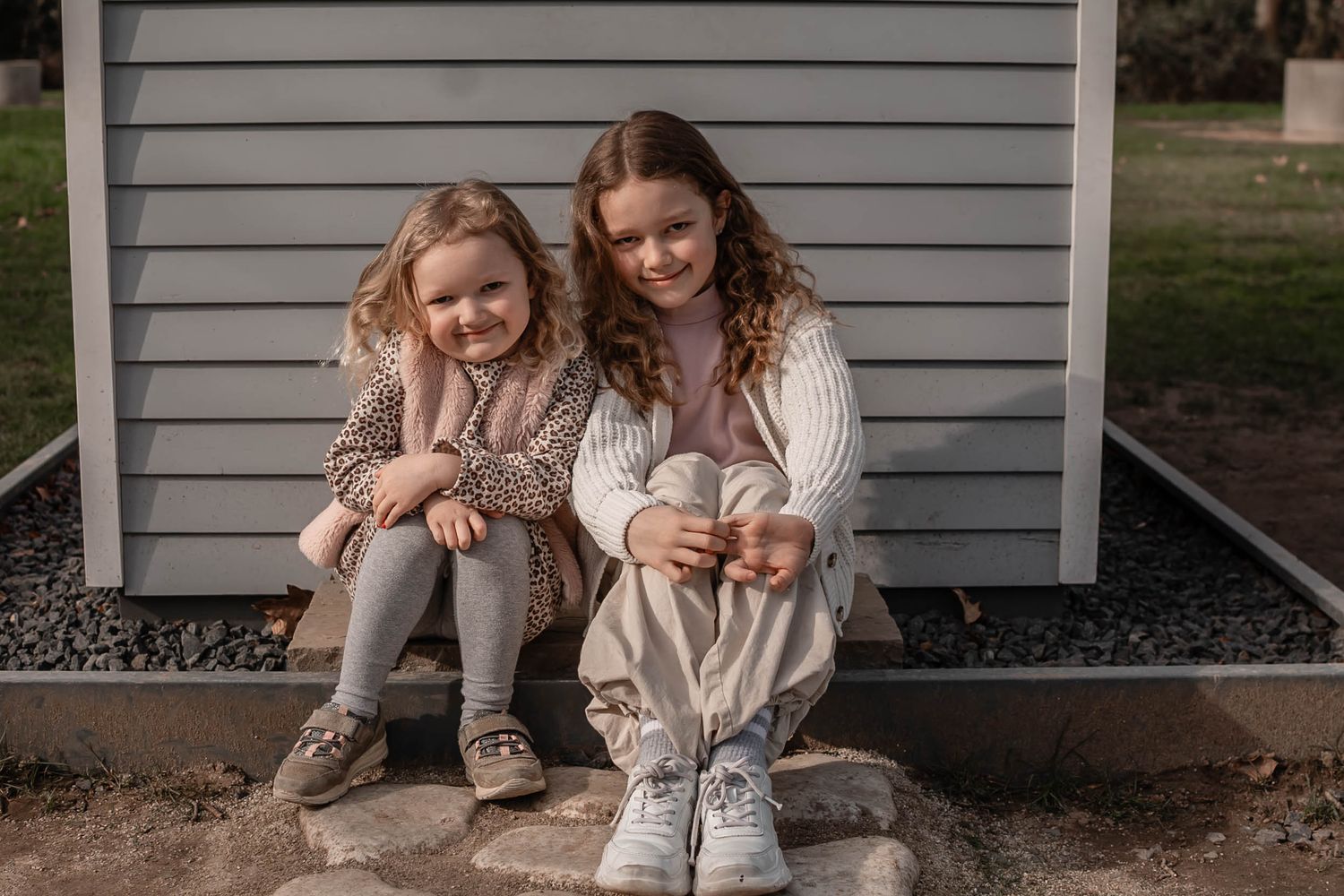 Two people in light colored sweaters sitting close together on stone steps against a gray wall.