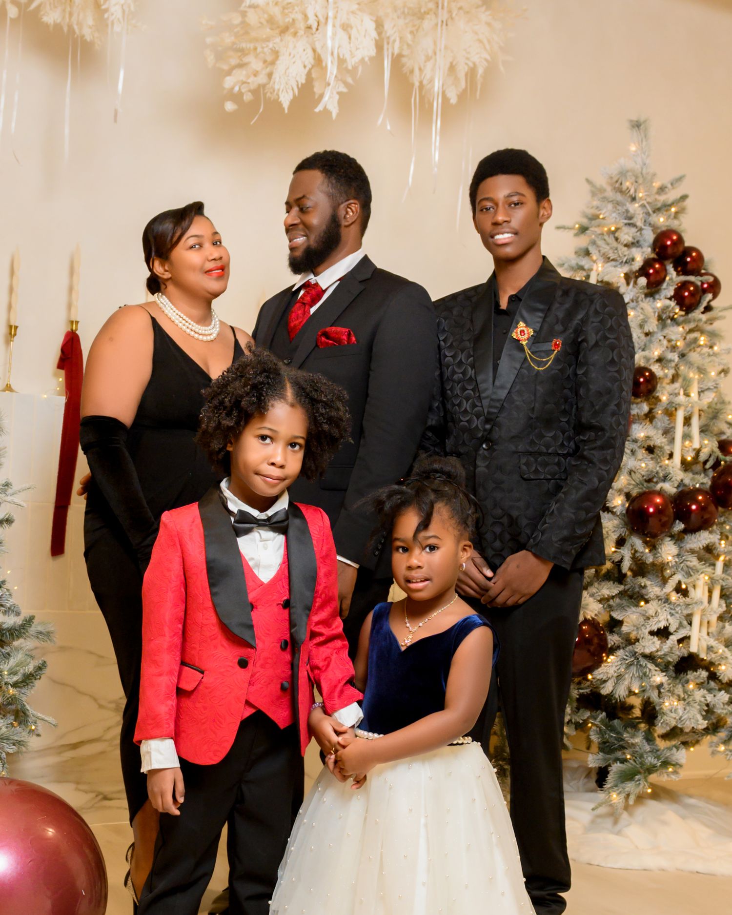 A festive holiday photo session with people in red and black formal attire posing in front of decorated Christmas trees.