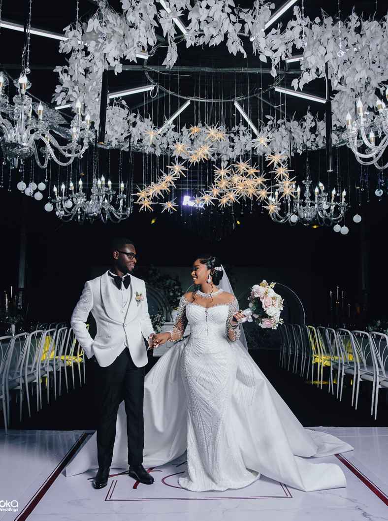 Elegant wedding reception setup with crystal chandeliers and modern white decor in a dramatic black venue.