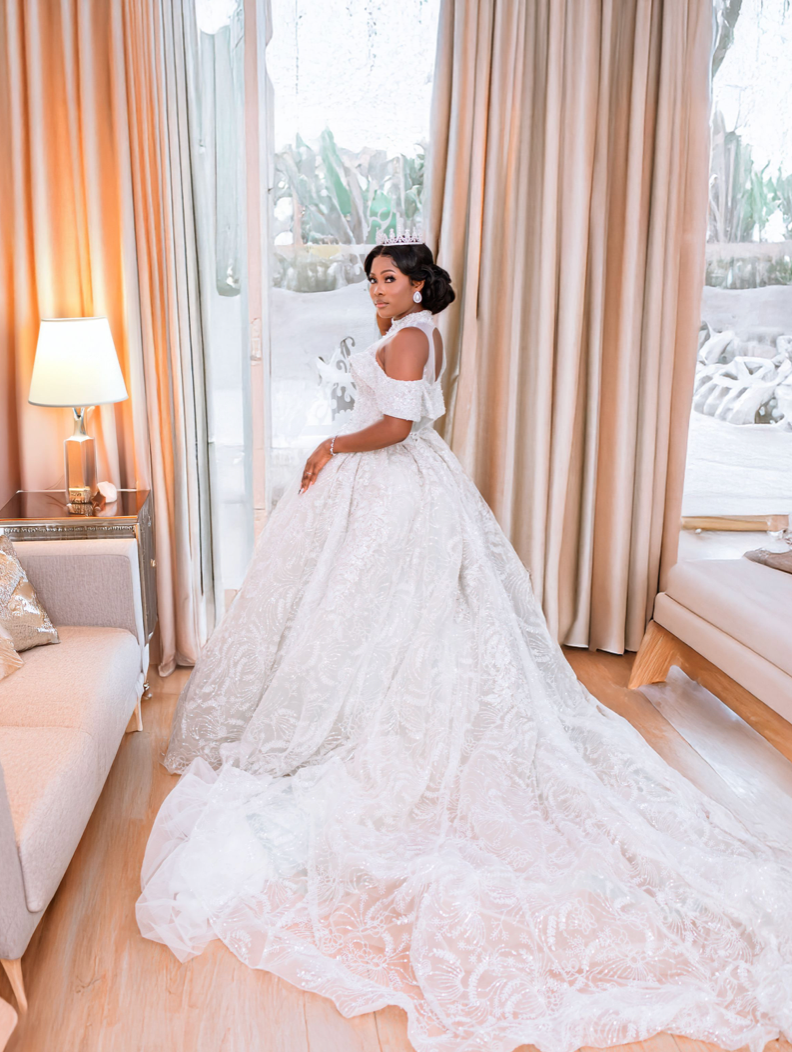 A stunning white ball gown wedding dress with a dramatic train photographed in an elegant room with cream curtains.