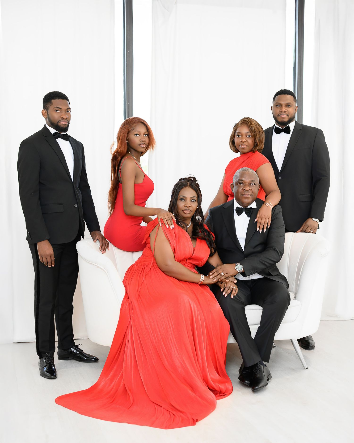 A formal family portrait featuring a group in black tuxedos and coral red dresses against a white backdrop.
