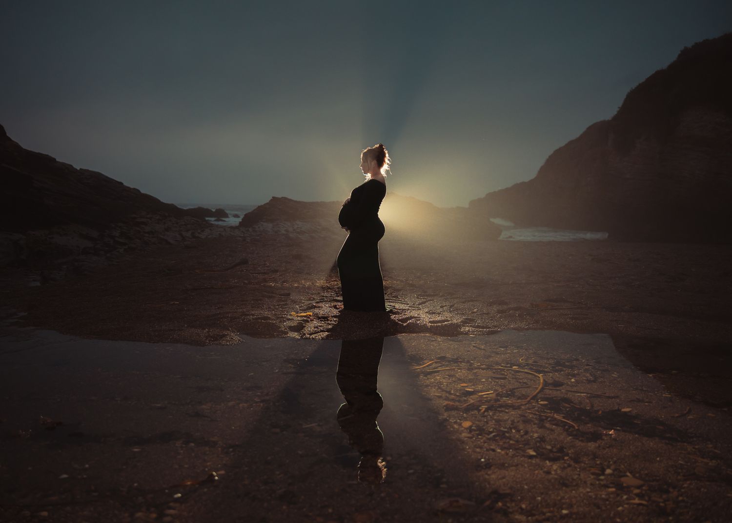 A silhouetted figure stands against a dramatic sunset on a rocky desert mountain ridge.