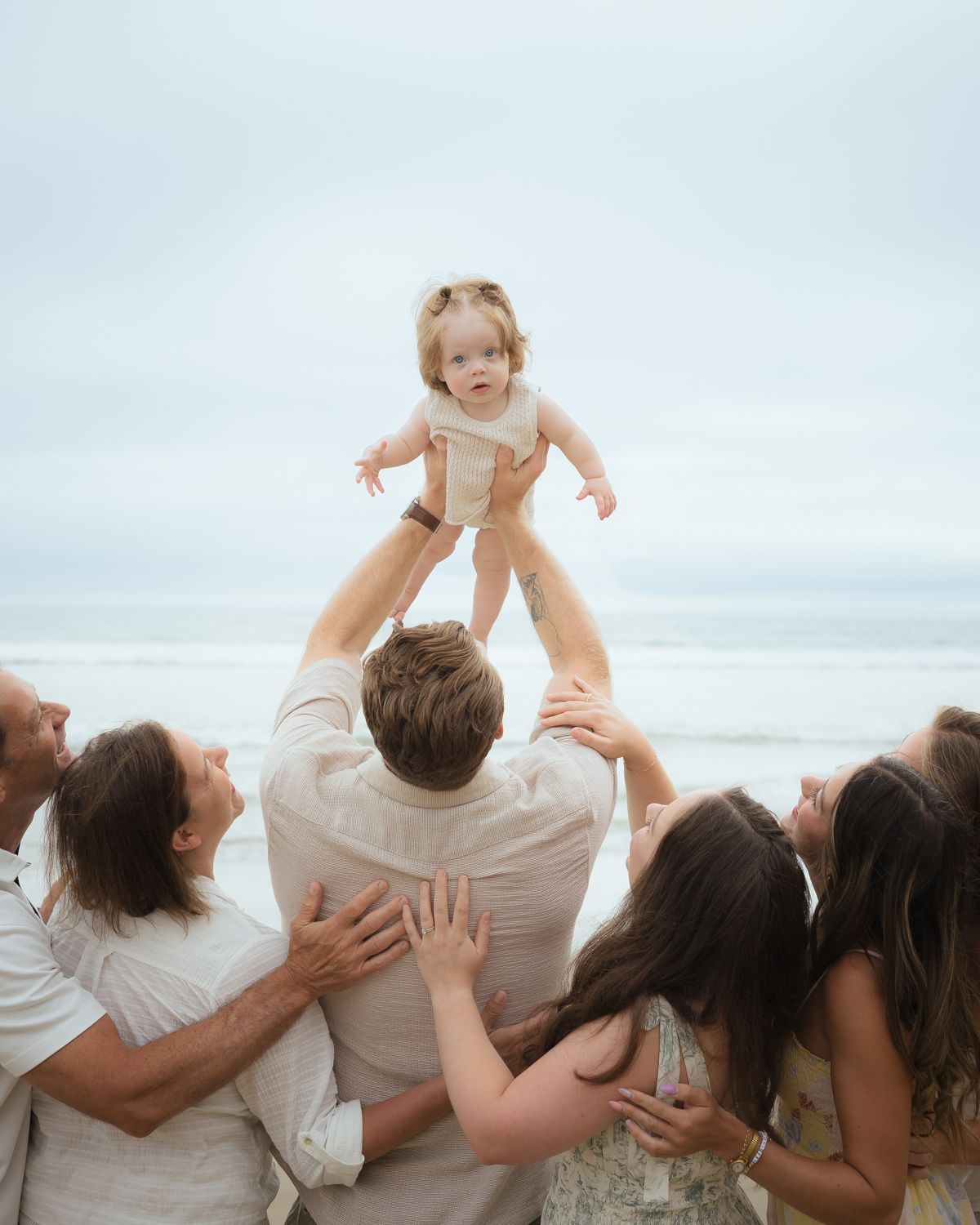 A heartwarming family beach photo with a baby being lifted up by loved ones.