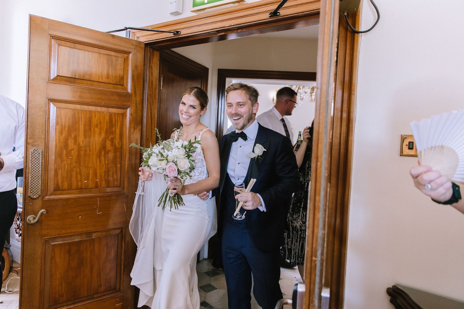 A joyous couple walks through a wooden doorway during their wedding ceremony, with the bride holding a white bouquet.