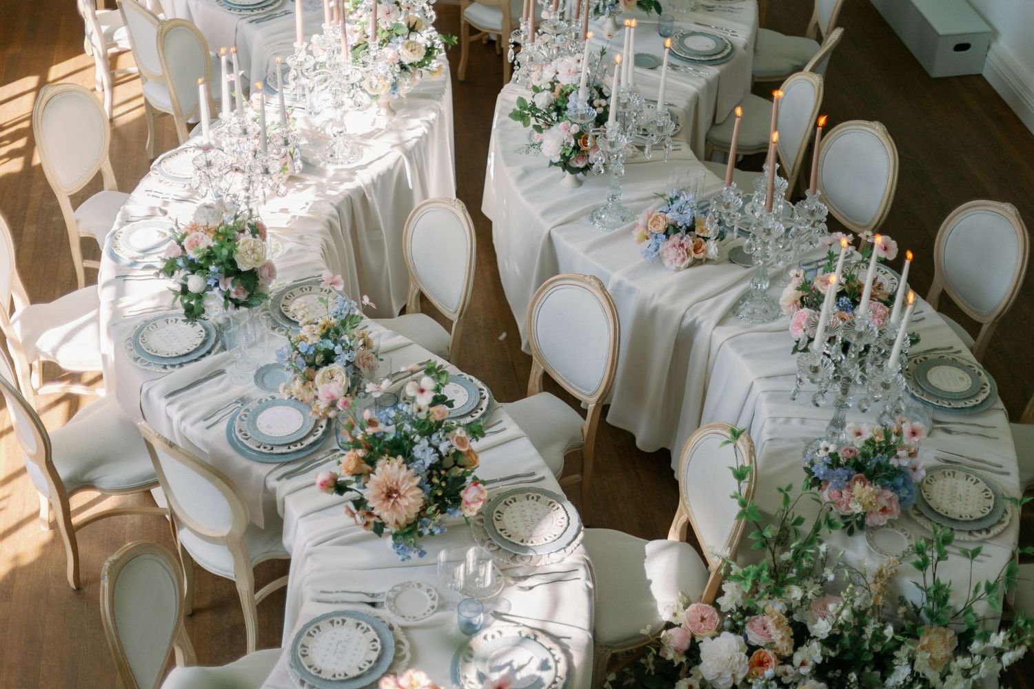 Elegant wedding reception tables with white linens, crystal glassware, and romantic floral centerpieces in blush and green tones.