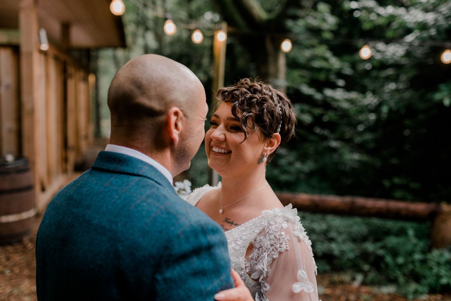 A couple shares intimate moments during a rustic outdoor wedding ceremony surrounded by trees and natural lighting.