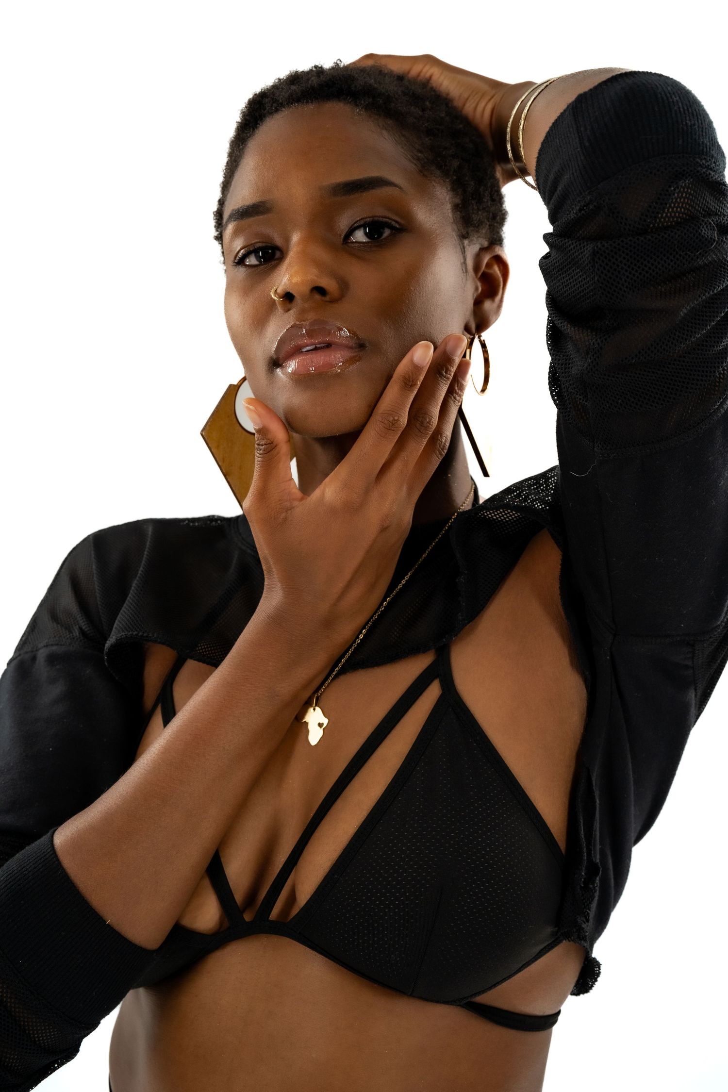 Artistic portrait shot wearing black outfit with gold jewelry against white backdrop.