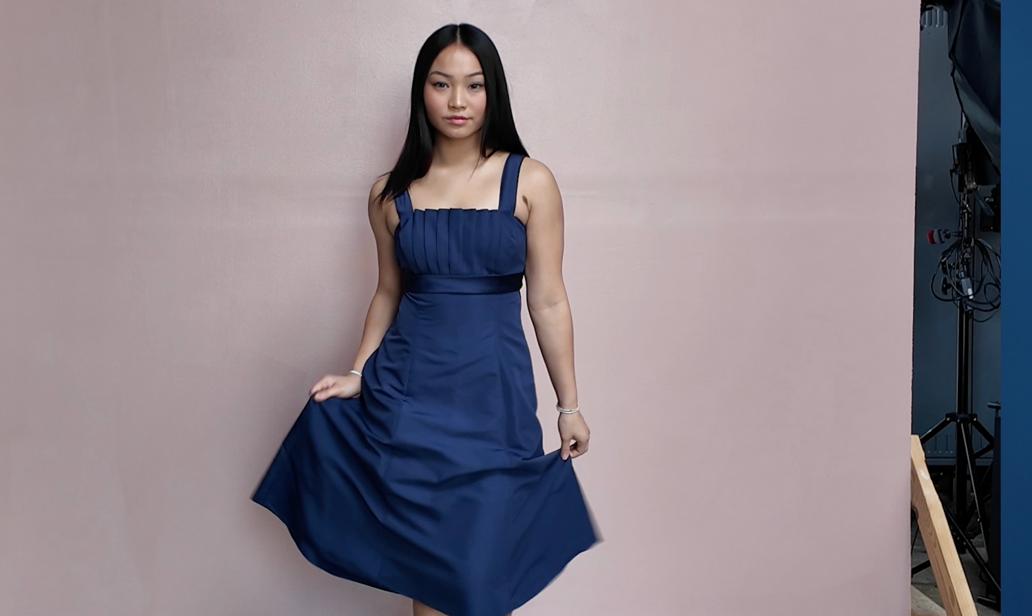 Woman in navy blue fit-and-flare dress poses against light pink wall.