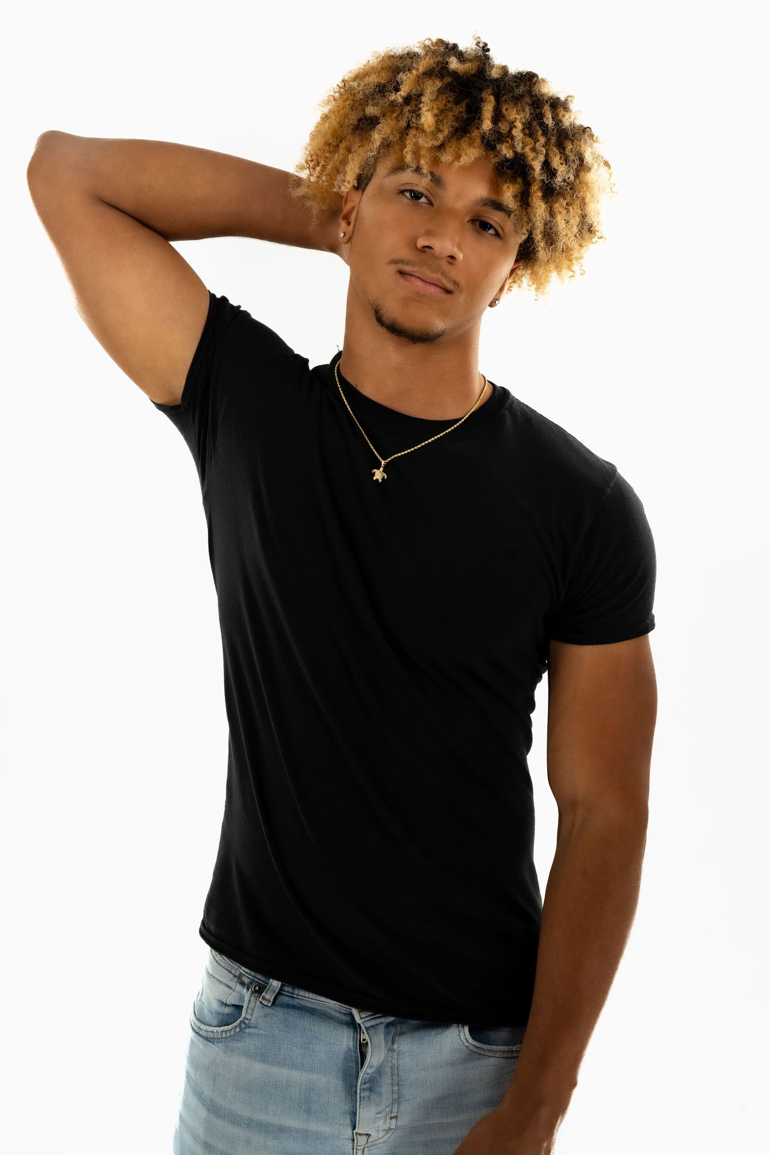 A fashion model poses in a casual black t-shirt and light wash jeans against a white background.