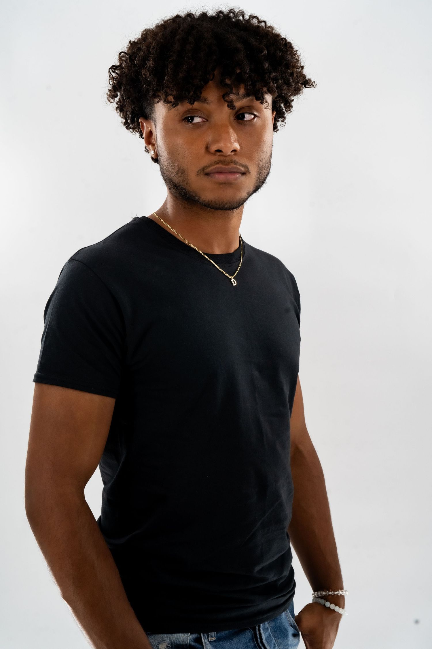 Studio portrait against white background wearing black t-shirt and silver necklace.