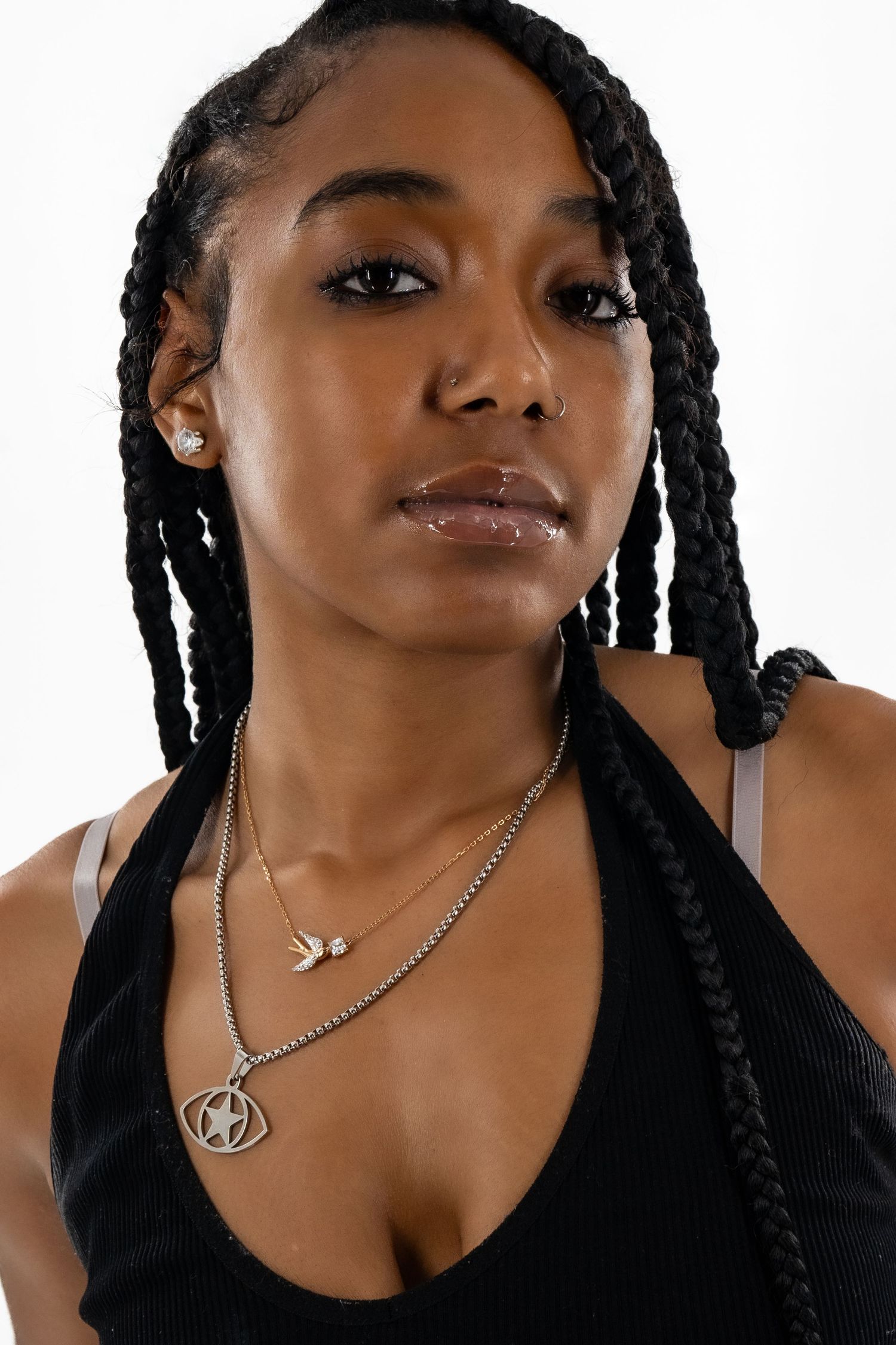 Close-up portrait featuring layered necklaces and black top against white background.