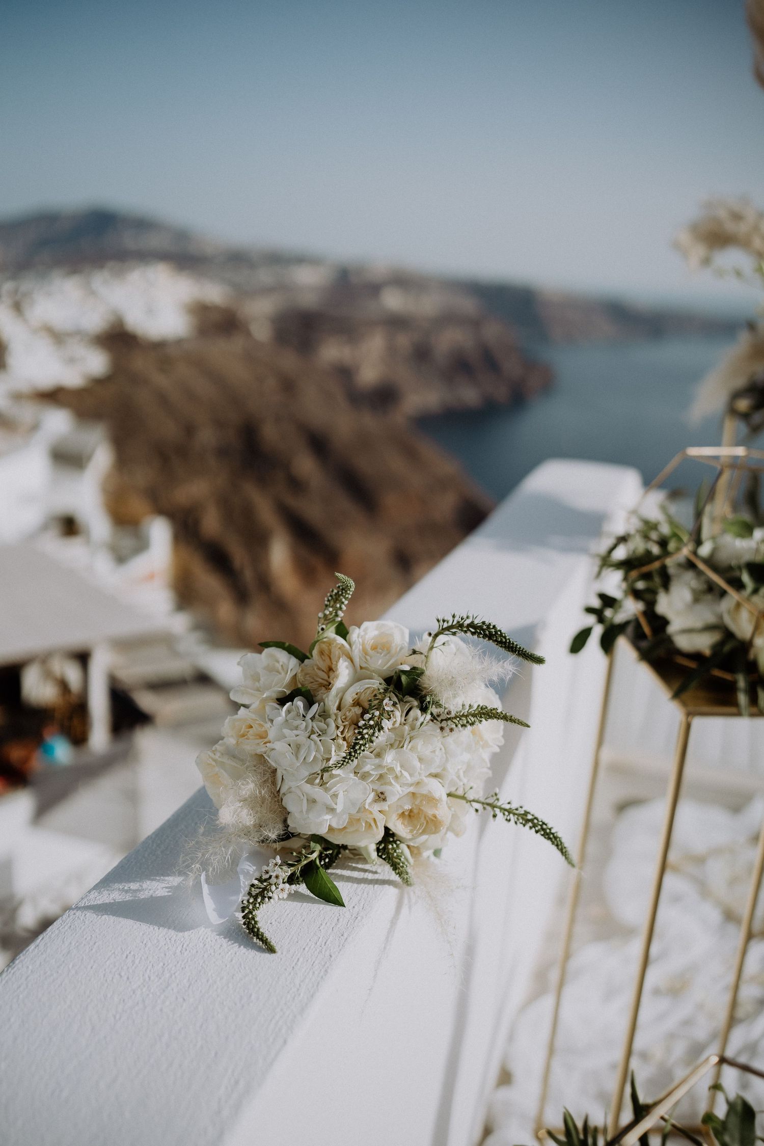 White floral arrangement with coastal views of Santorini's dramatic caldera landscape.