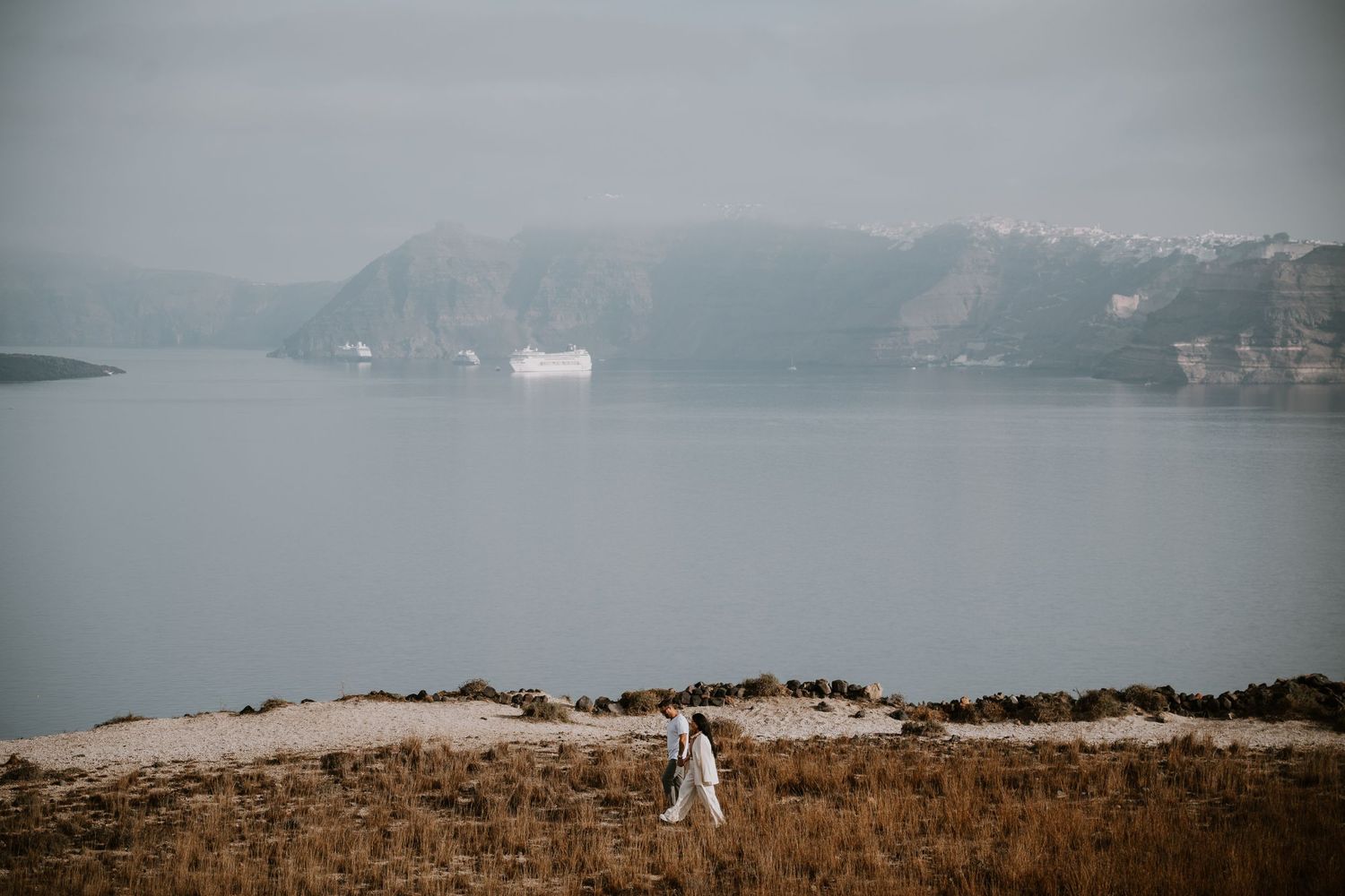 Misty coastal landscape with dramatic cliffs and distant ships on the water.