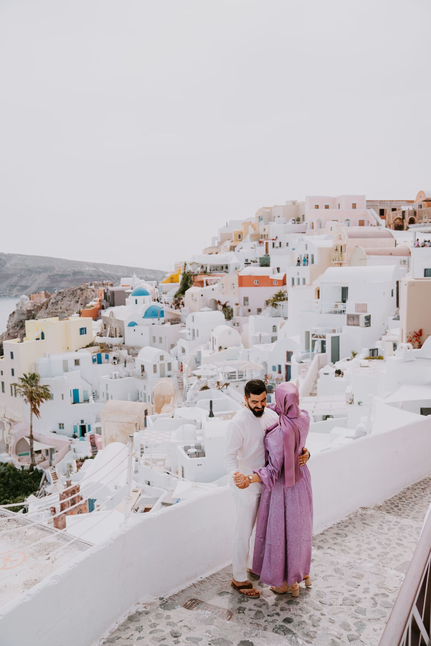 A couple standing in the white-washed streets of Santorini among traditional Greek architecture.