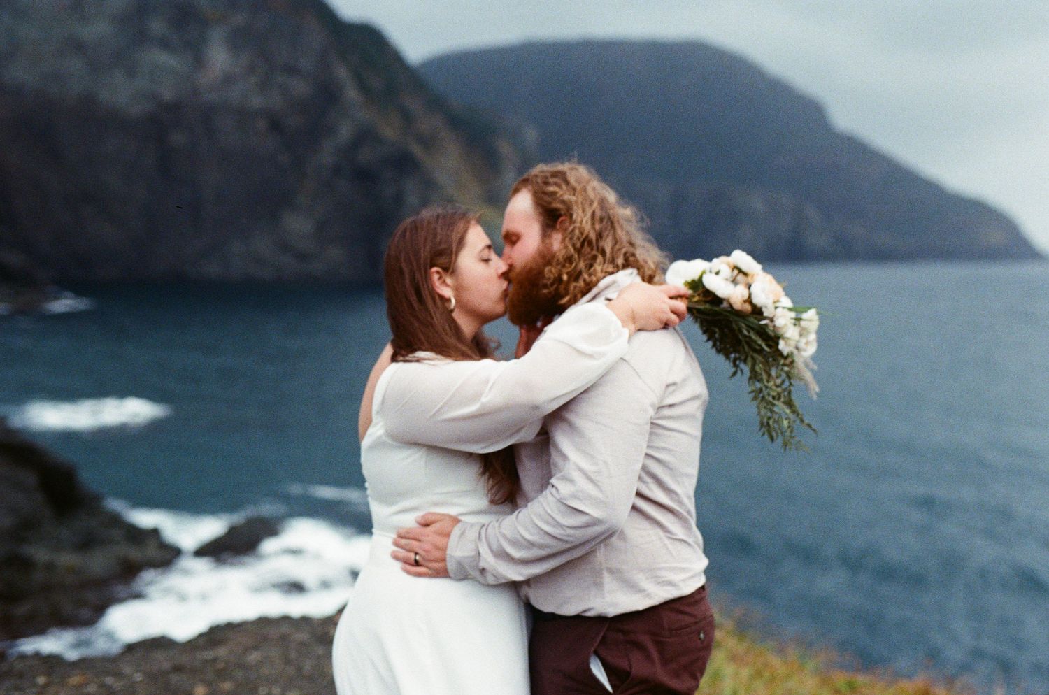 35 mm film photo of bride and groom kissing on the stormy coast during their Tofino Elopement
