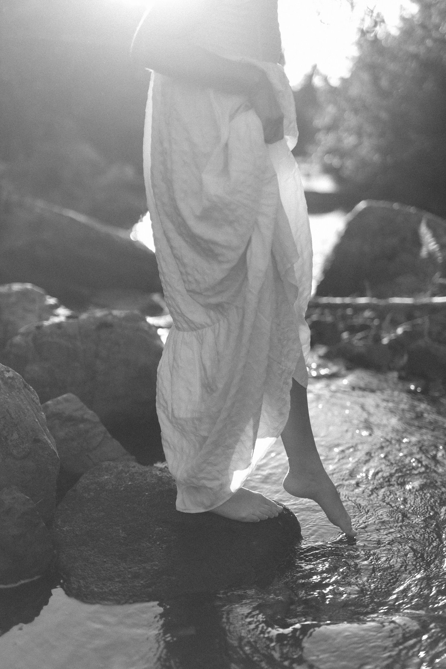 woman gathers up her long skirt to dip her toes in a river during her Self Love Session