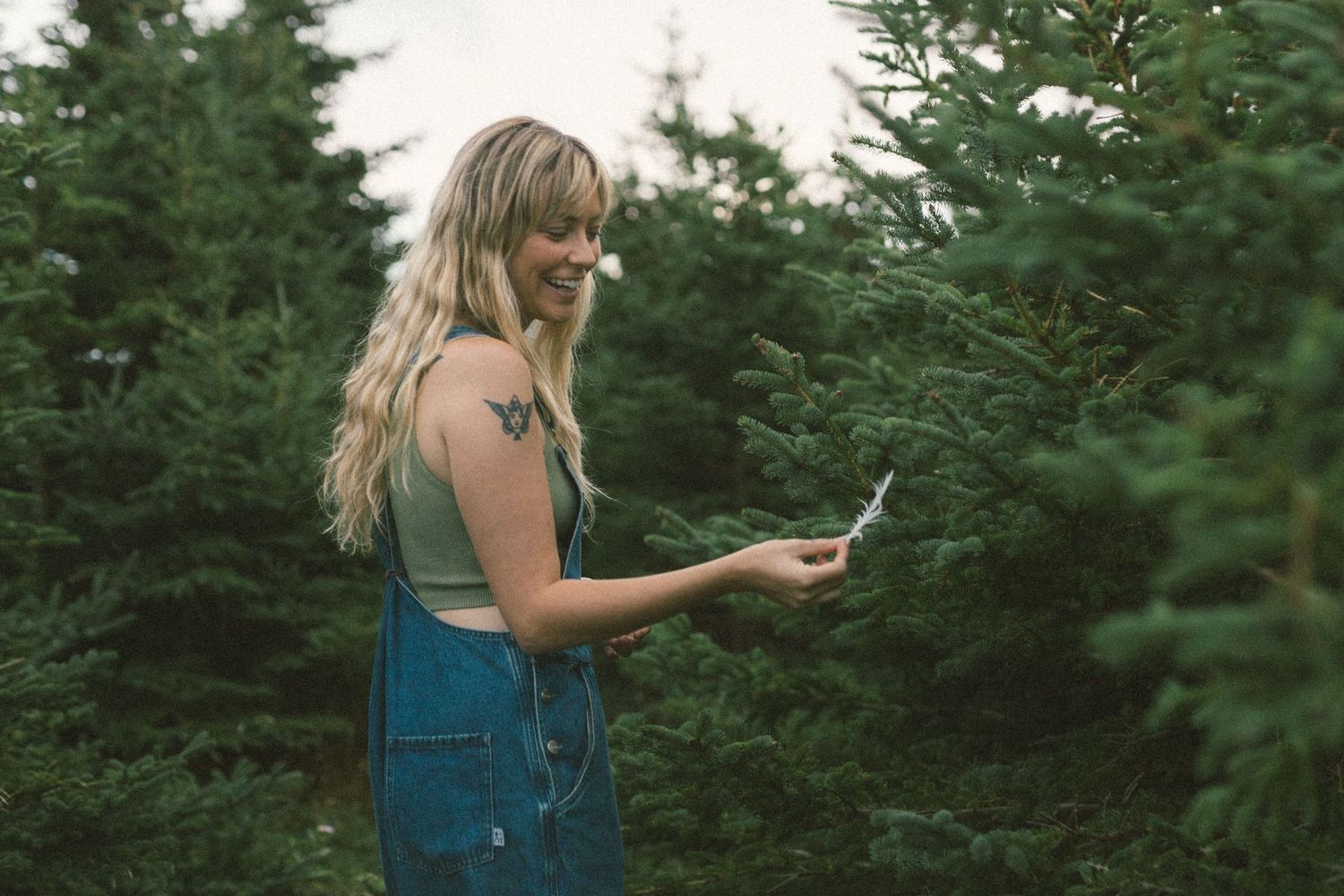 woman laughs as she picks up a feather in the forest during her Self Love Session