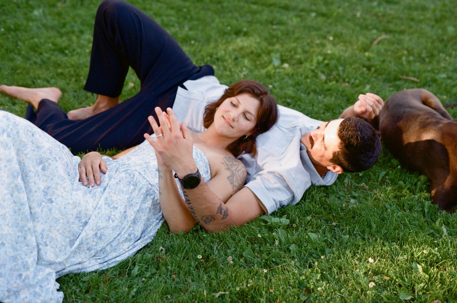 35 mm film photo of a couple laying in the grass in dappled sunlight intertwining their fingers together