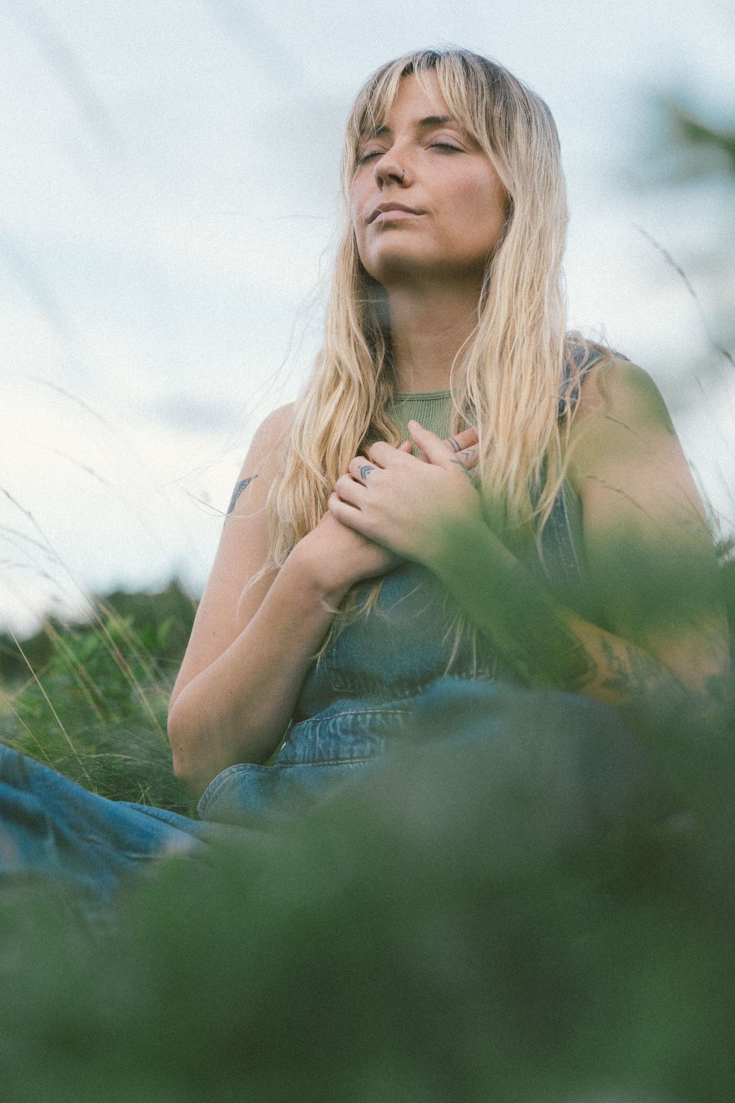 blonde woman with tattoos meditates in a wild meadow during Self Love Session