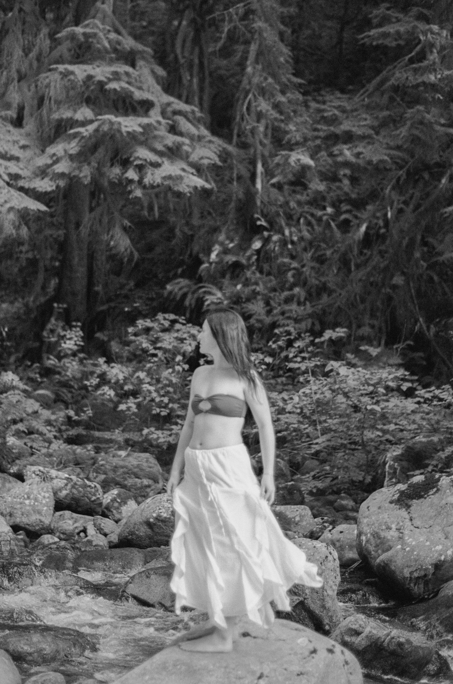 woman twirls on a rock in the river so her long white skirt flows around her