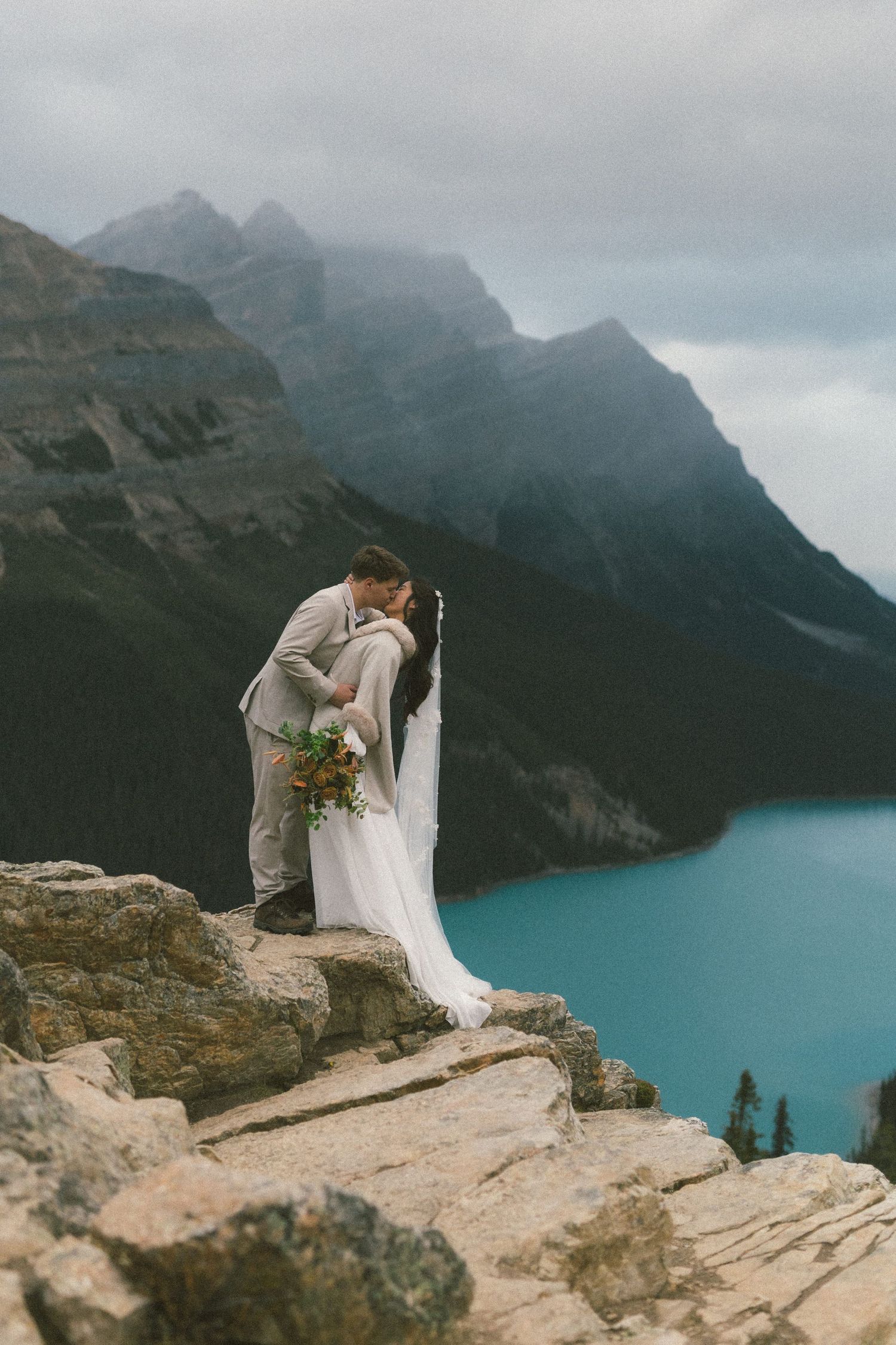 bride and groom kiss on a rocky outcrop above a mountain lake in Banff