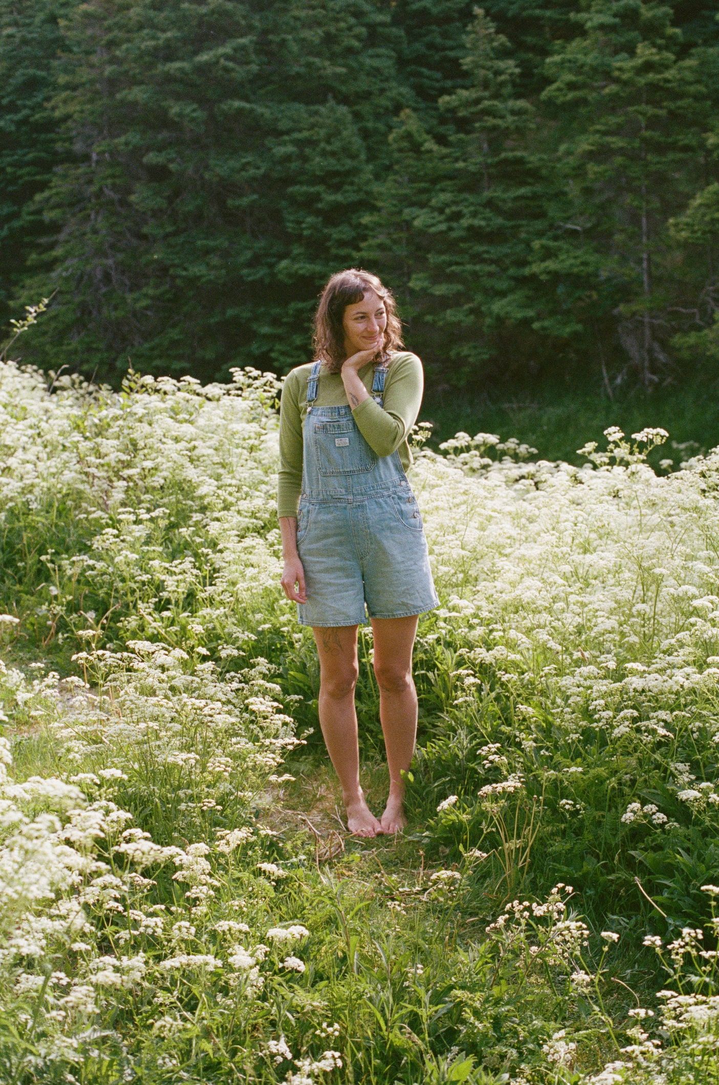 35 mm film photo of Banff Elopement Photographer Heather Nolan standing in a field of wildflowers in denim overalls