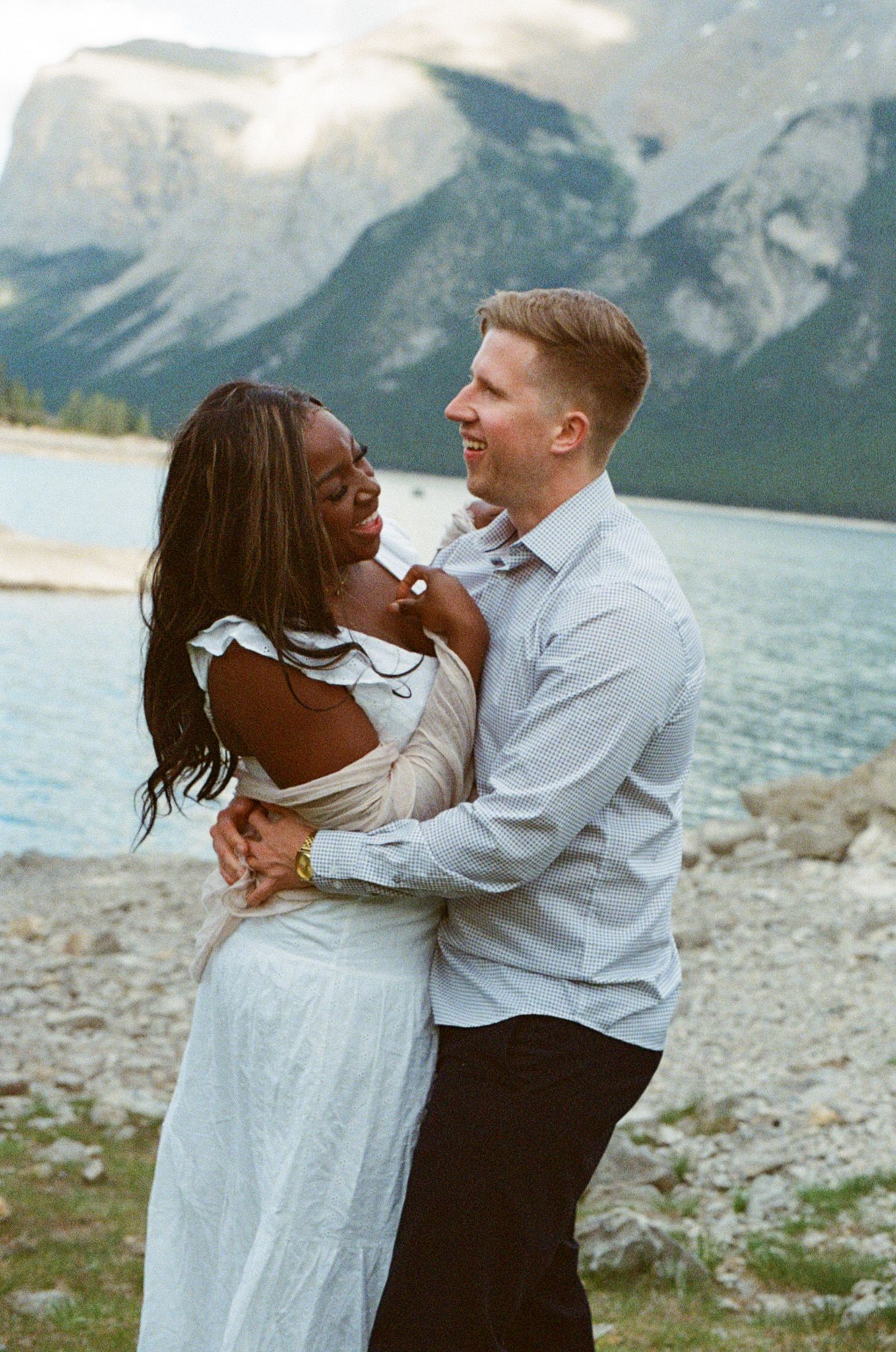 35 mm film photo of an interracial couple holding each other and laughing at Lake Minnewanka in Banff National Park