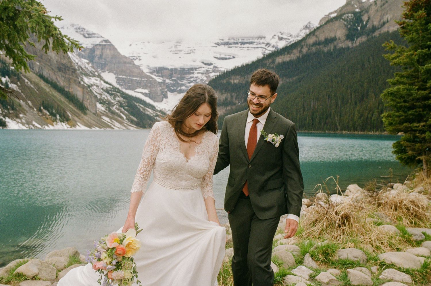 35 mm film photo of bride and groom walking away from the lakeshore at Lake Louise during their Banff Elopement