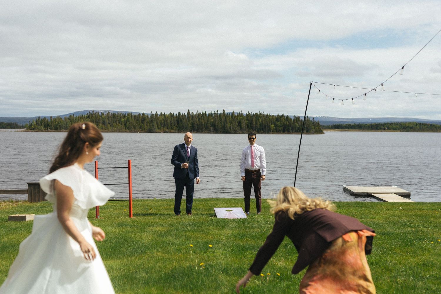 bride and groom play lawn games with their siblings by a lake