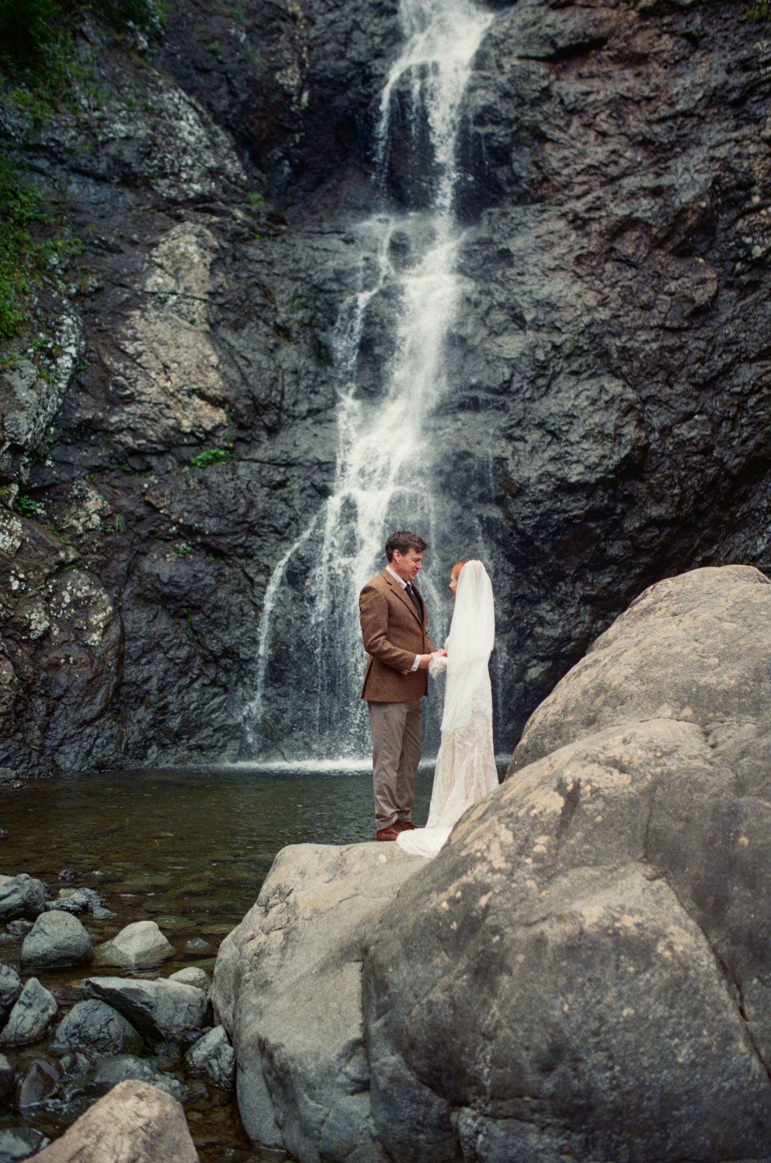 35 mm film photo of a bride and groom quietly talking beside a waterfall on their elopement day