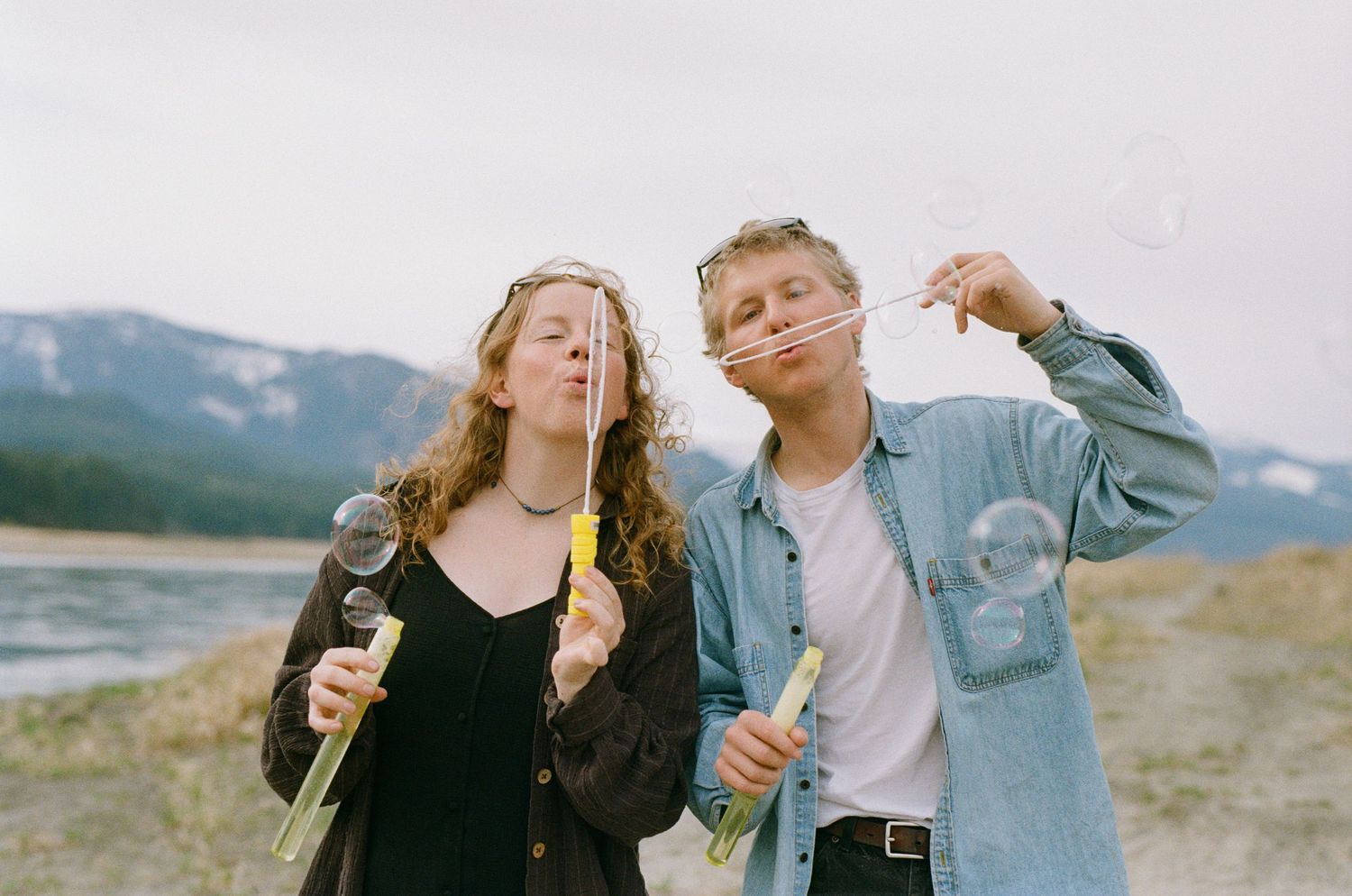 35 mm film photo of a couple in casual clothes blowing bubbles by a river
