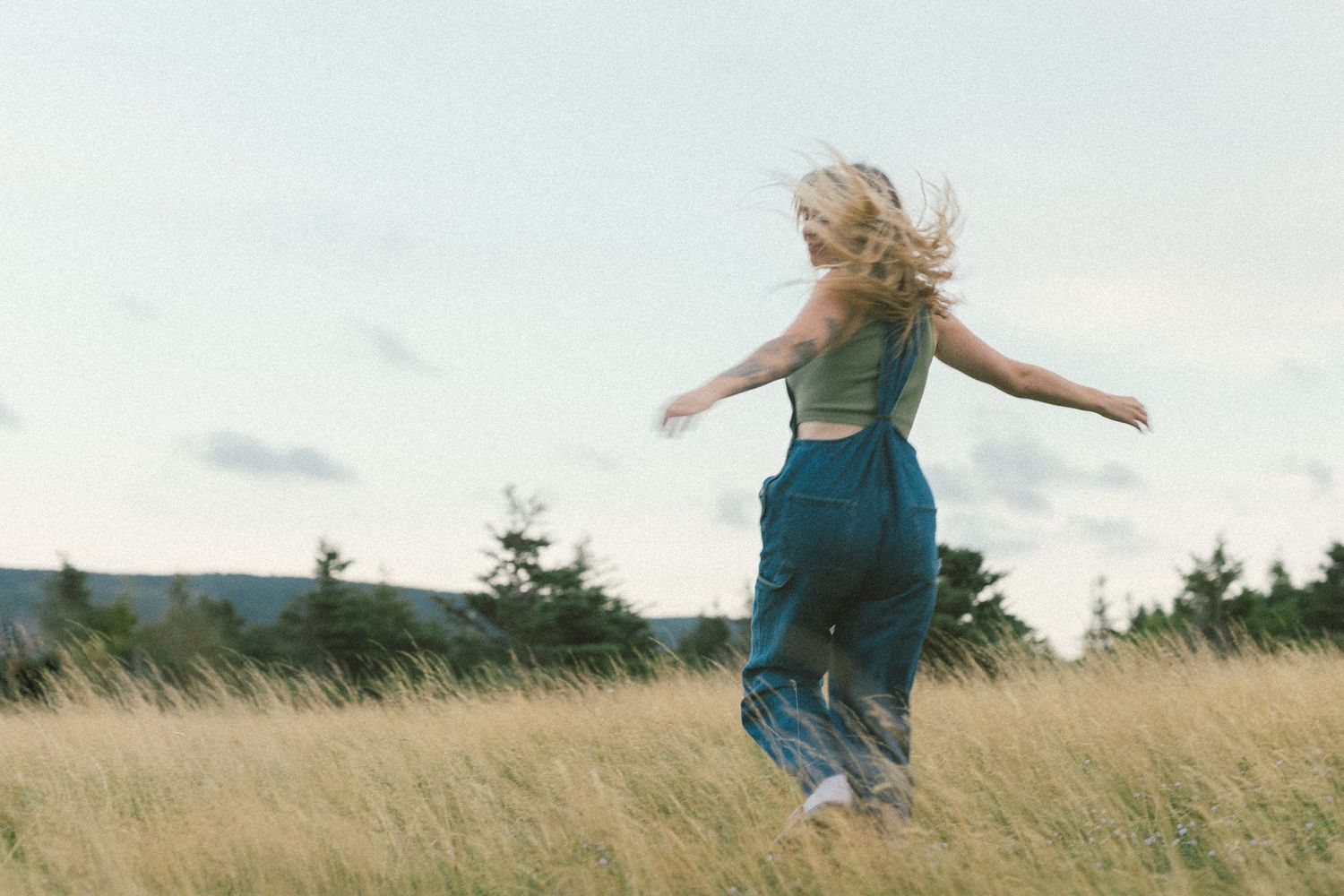 35 mm film photo of a woman twirling in a meadow with her hair blowing in the wind
