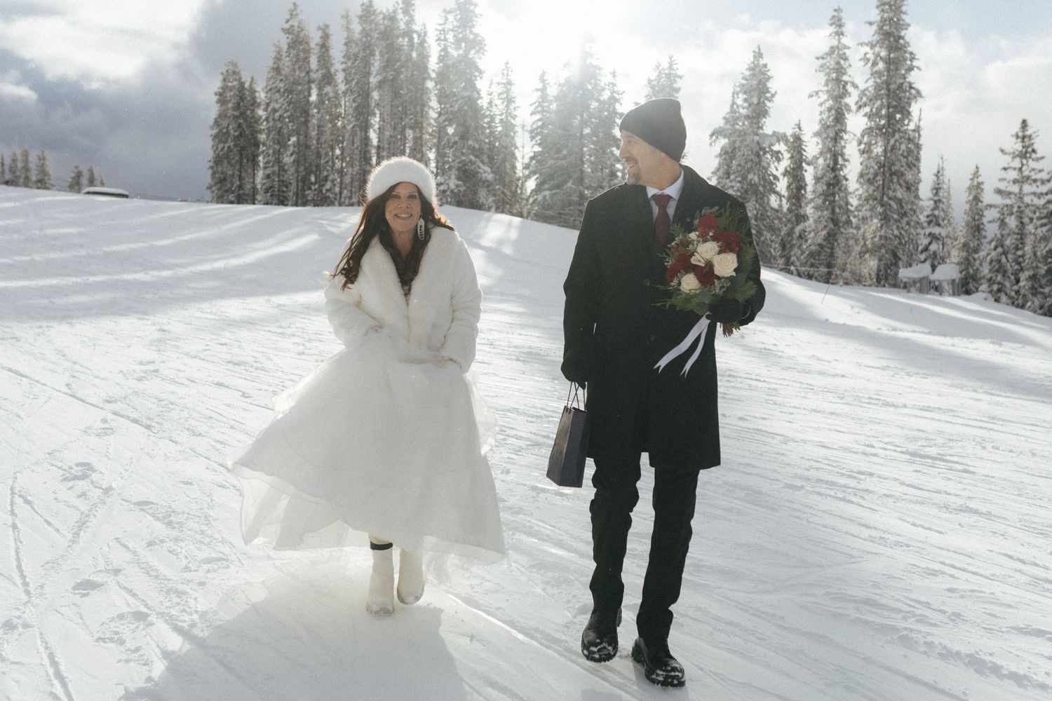 bride and groom walk across snowy ski run toward their Revelstoke Mountain Resort elopement ceremony location