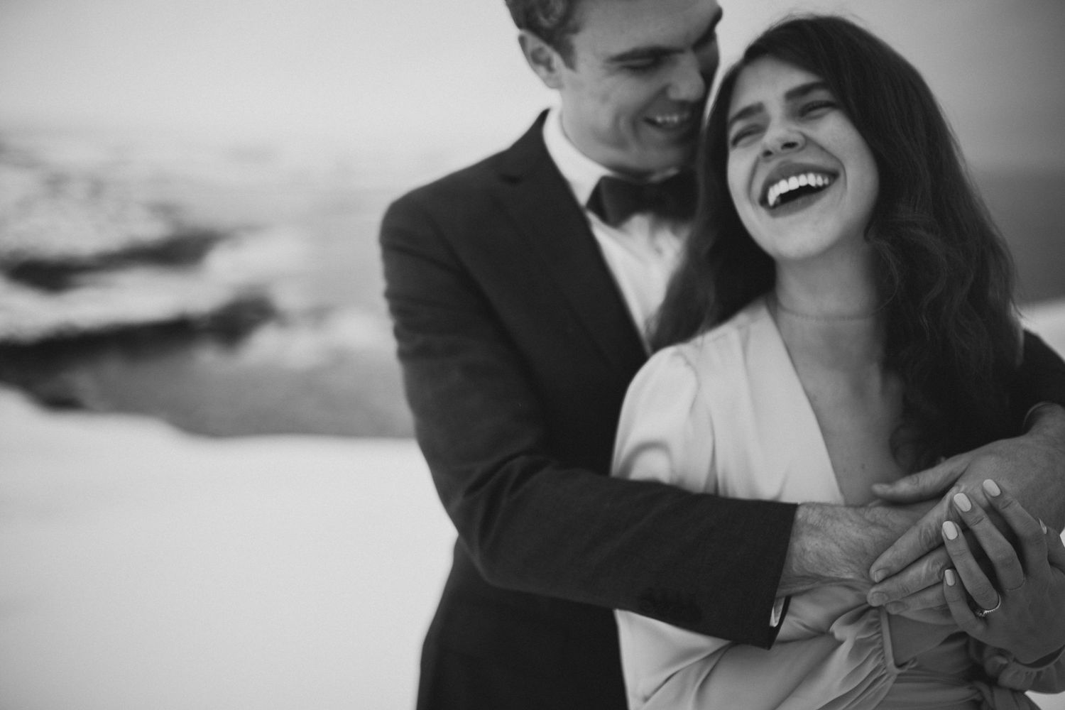 bride and groom hold each other and laugh in a snowy barren landscape