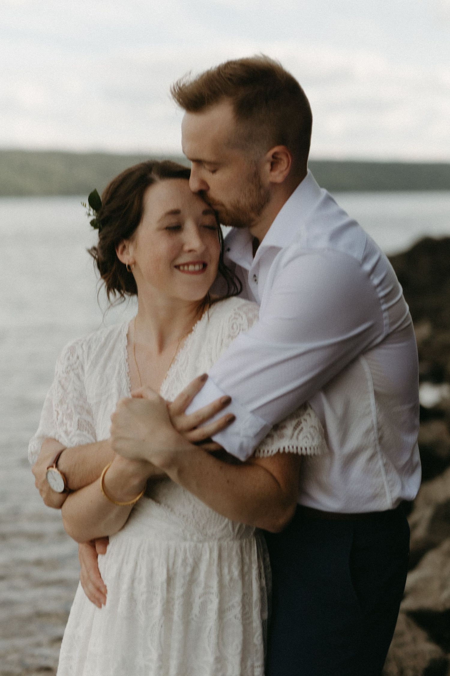 bride and groom hold each other beside a calm lake