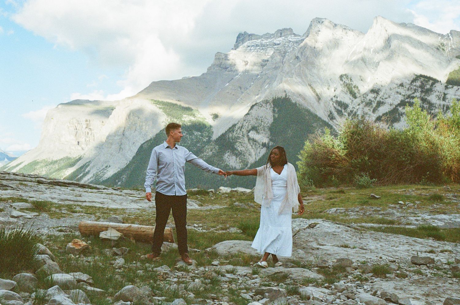 35 mm film photo of a mixed race bride and groom walking along a rocky lakeshore in Banff with mountain views