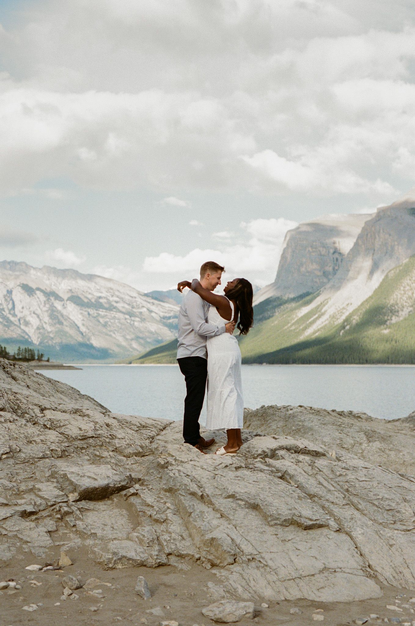 35 mm film photo of a bride and groom cuddling on the rocky shore of Lake Minnewanka in Banff National Park