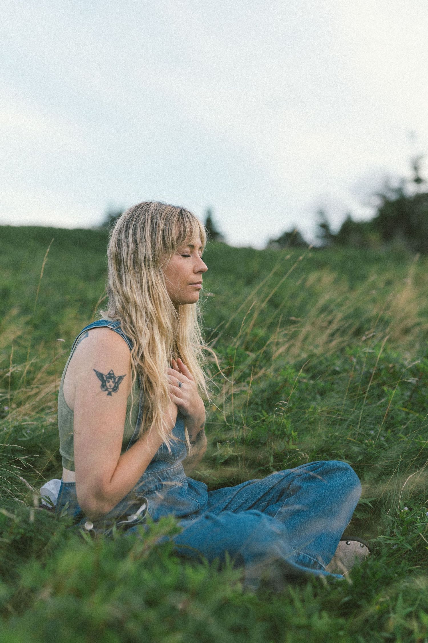 blonde woman with tattoos meditates in a wild meadow during Self Love Session