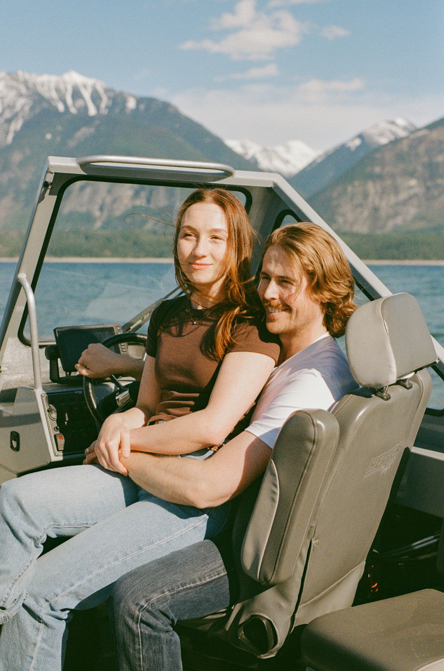 35 mm film photo of a couple laughing on their speed boat in the sun on a lake in the mountains in BC