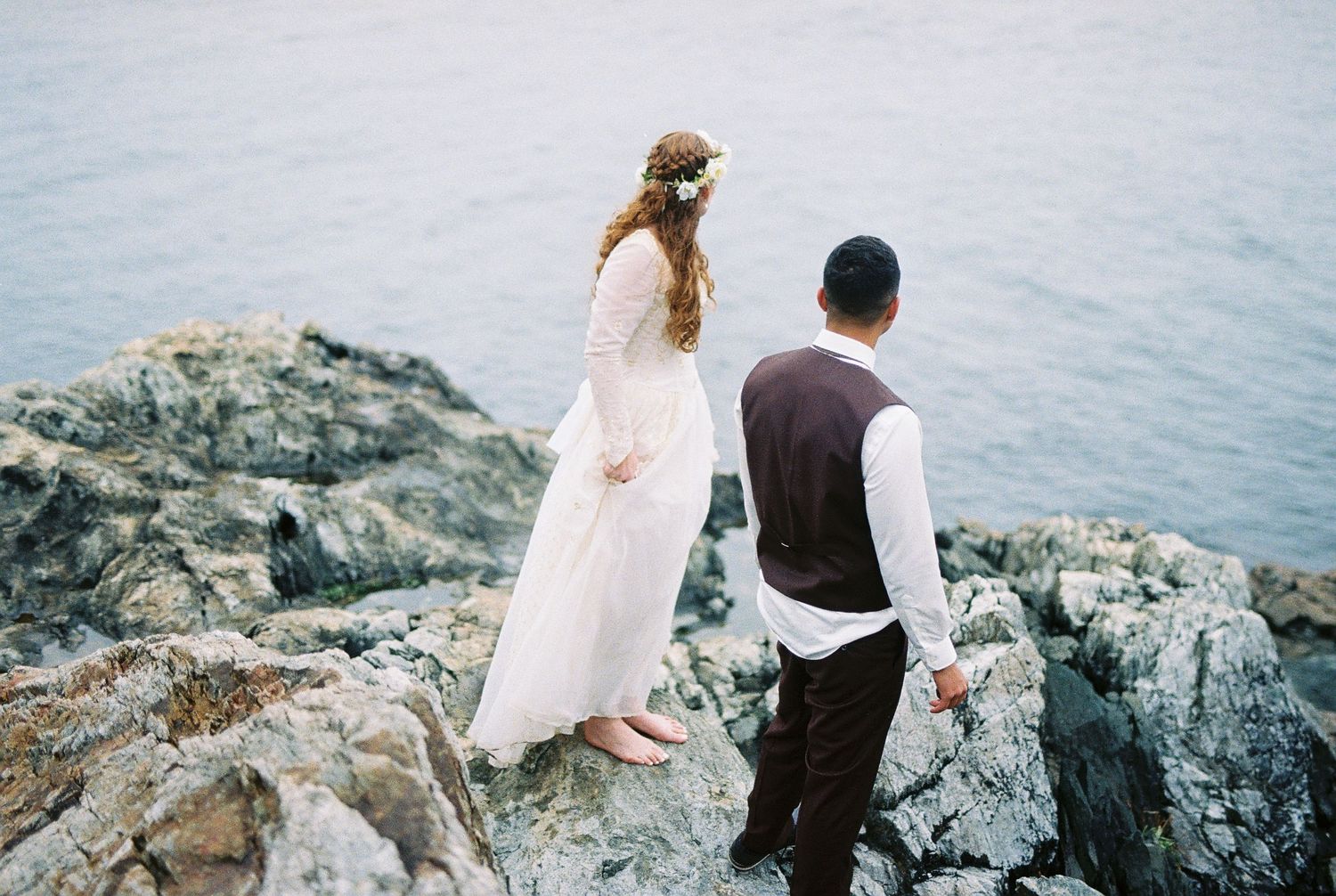 35 mm film photo of bride and groom walking along rocky shore barefoot during their Tofino Elopement
