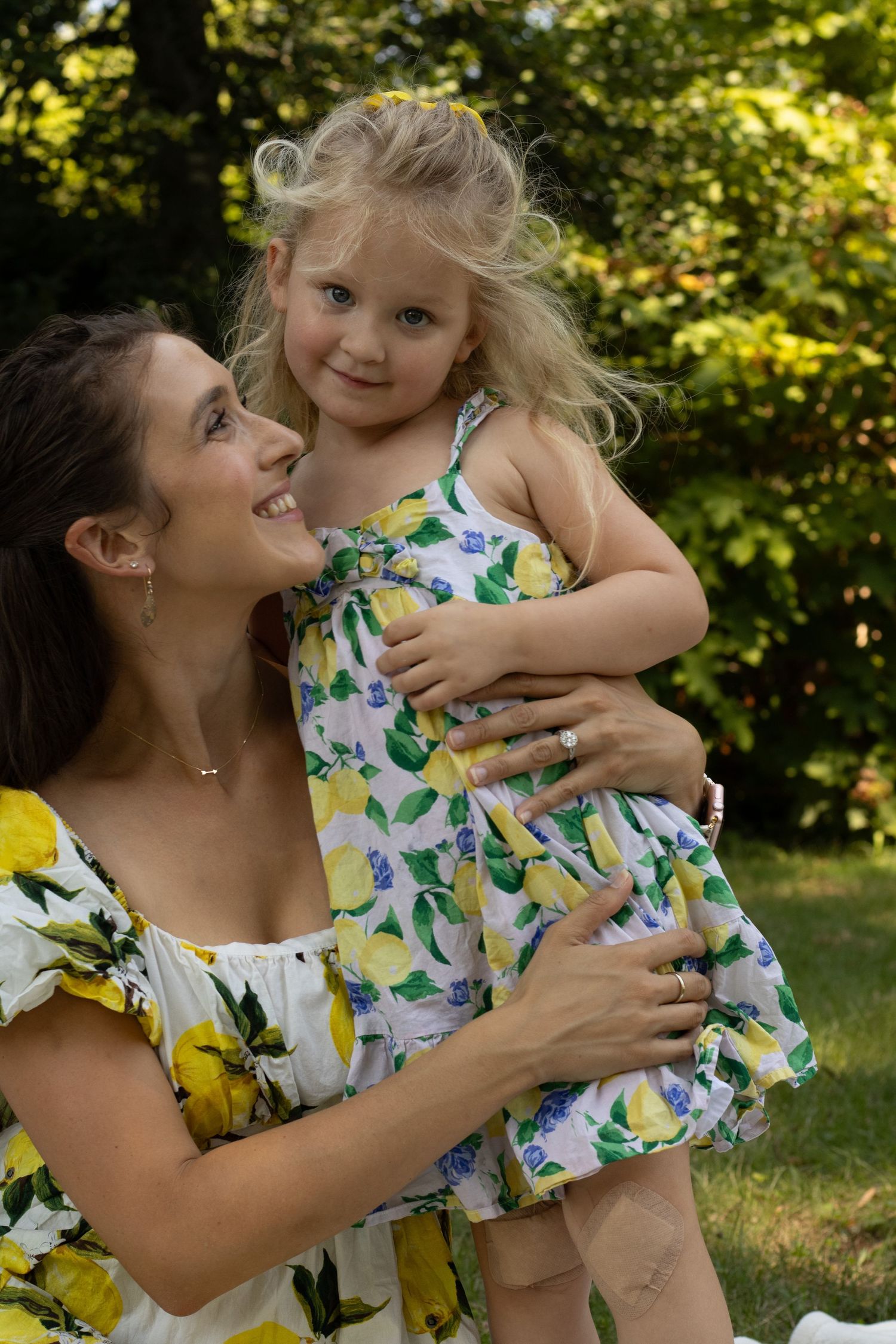 Mother and daughter wearing matching floral dresses share joyful moments together in a sunny garden setting.