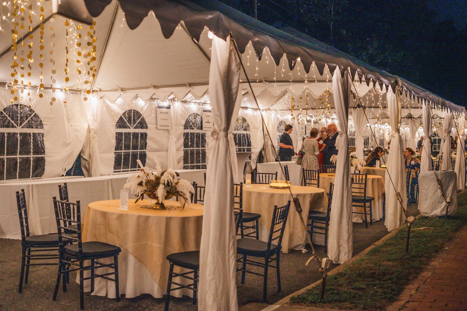 White wedding tents illuminated at night with elegant string lights and chairs set up for an outdoor reception.