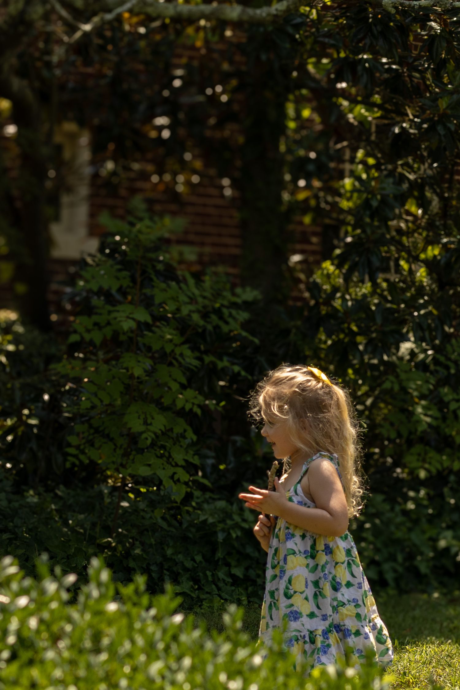 A small child in a floral sundress stands in a sunlit garden with floating bubbles in the air around them.
