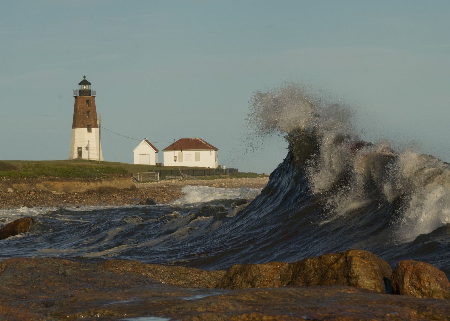A massive wave crashes against rocks near Point Judith Lighthouse in Rhode Island during stormy weather.