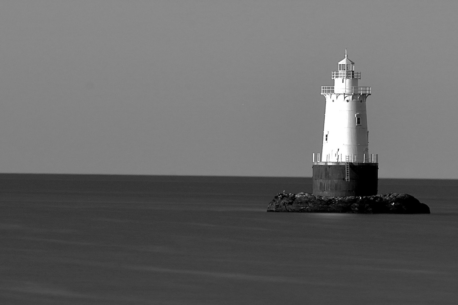 Minimalist view of a lighthouse rising from the horizon over calm waters.